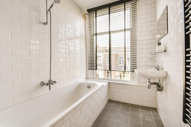 Foto un baño blanco con azulejos negros y blancos en el suelo bañera ducha y ventana en el fondo