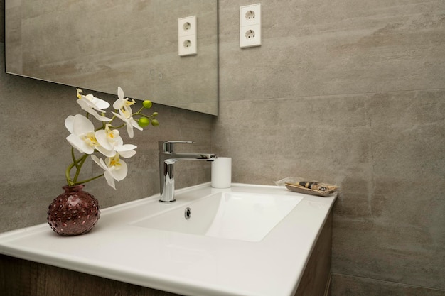 Baño con cajonera de roble con azulejos de mármol de imitación gris, espejo de pared sin marco, accesorios de acero inoxidable, lavabo de porcelana blanca