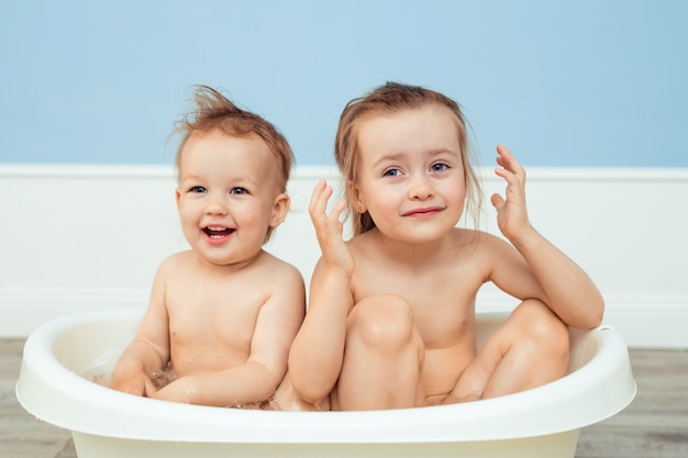 baño e higiene para bebés. cuidado de niños pequeños. dos hermanas alegres se bañan en una bañera blanca y juegan entre la espuma de jabón