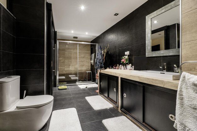 Foto baño grande totalmente revestido de azulejos con azulejos de pizarra negra unidad de vanidad de madera negra encimera de mármol
