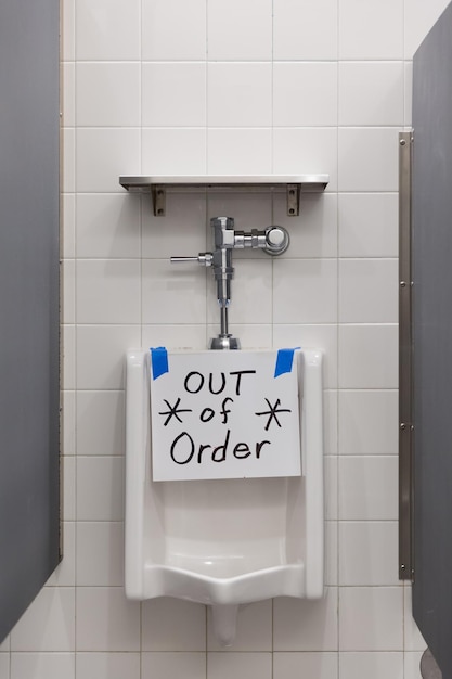 Baño público para hombres y inodoro roto en el baño masculino con letrero fuera de servicio