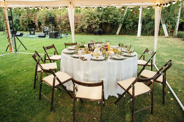 Banquete de bodas Las sillas y la mesa redonda para invitados se sirven con cubiertos, flores verdes y vajilla y se cubren con un mantel blanco color oliva