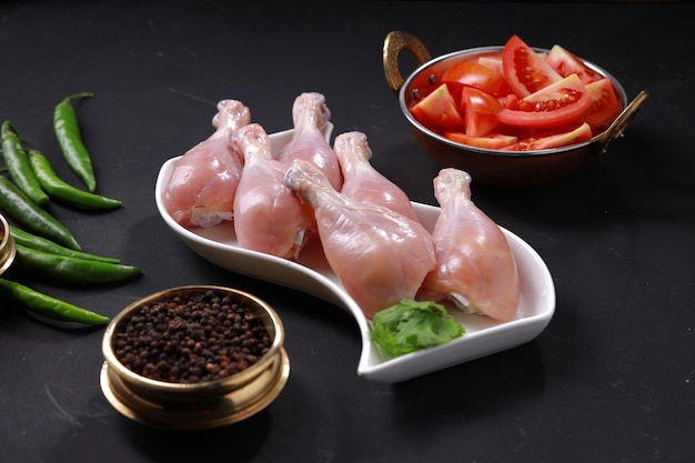 Baqueta de frango cru ou pedaços de perna dispostos em utensílios de mesa brancos com fundo cinza.