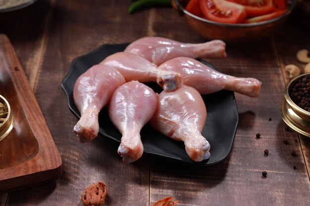 Baquetas de frango cru dispostas em utensílios de mesa pretos com ingredientes de cozinha colocados nas proximidades