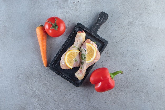 Baquetas y rodajas de limón sobre una tabla junto a verduras, en la superficie de mármol.