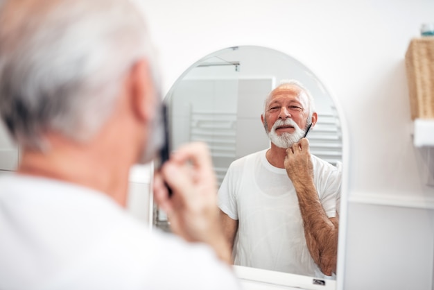 Barba de aliciamento. Homem sênior que penteia sua barba no banheiro.