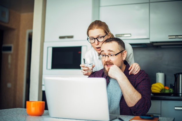Barba hombre y mujer con gafas en la cocina mirando la computadora portátil discutiendo las noticias de la mañana Pareja adulta pasando tiempo juntos en casa