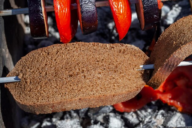 Barbacoa con cocción al fuego de berenjena fresca y tomate y berenjena de pan de centeno cortada en trozos mientras se cocina en la barbacoa