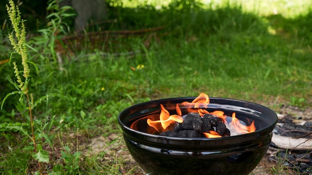 Barbacoa redonda negra con fuego al aire libre contra la hierba verde al aire libre