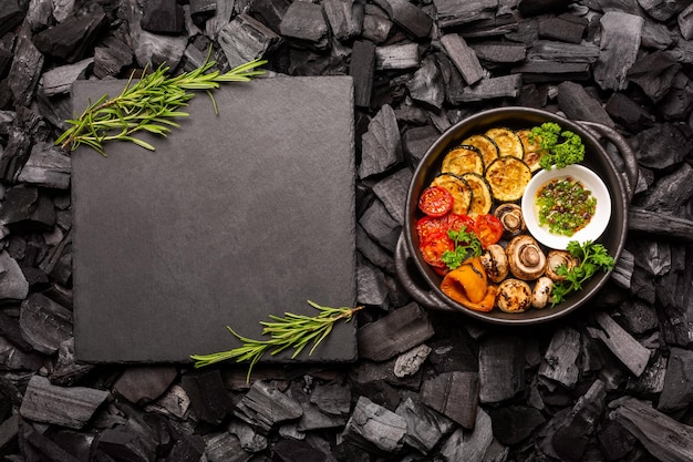 Foto barbacoa de verduras en una sartén y una tabla de piedra para cortar sobre carbones marco para receta o menú