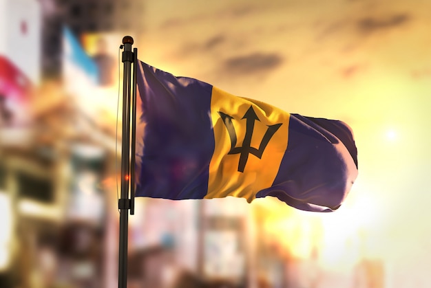 Barbados-Flagge gegen Stadt verschwommen Hintergrund bei Sonnenaufgang Hintergrundbeleuchtung