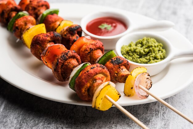 Foto barbecue oder tandoori pilz tikka, serviert in einem teller mit grünem chutney und ketchup. selektiver fokus