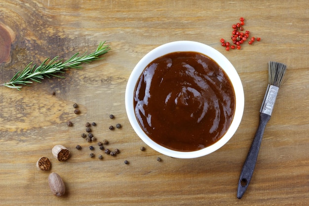 Barbecue-Sauce in Schüssel und Pinsel auf rustikalen Holztischgewürzen und Kräutern