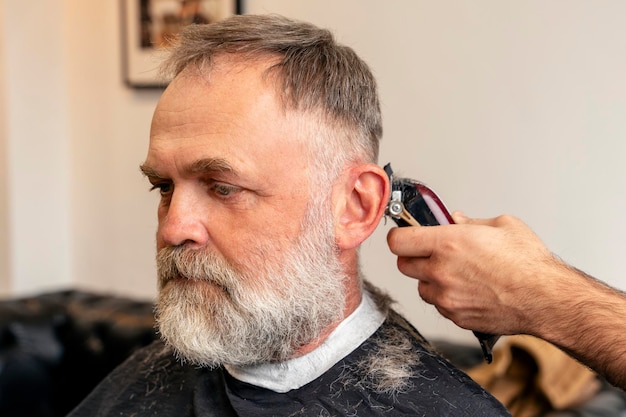 Barbeiro aparando e cortando homem barbudo com máquina de barbear no processo de penteado de barbearia