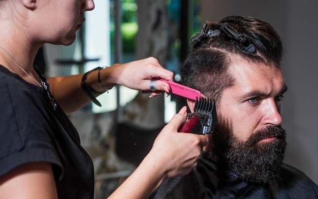 Barbeiro atraente fazendo corte de cabelo de homem bonito em ferramentas de cabeleireiro de barbearia