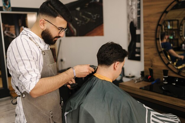 Barbeiro barbudo cortando cabelo de cabeleireiro cliente masculino atendendo cliente na barbearia