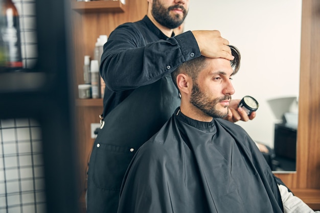 Barbeiro bonito em pé atrás de sua cliente e penteado depois de cortar o cabelo