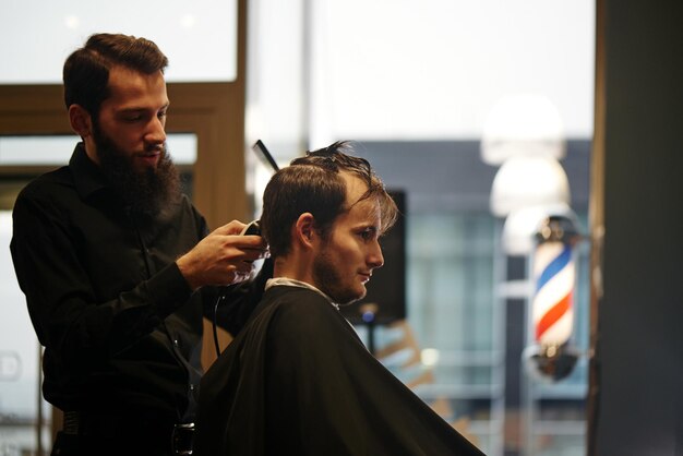 Barbeiro cortando a tesoura de cabelo de um cliente na barbearia