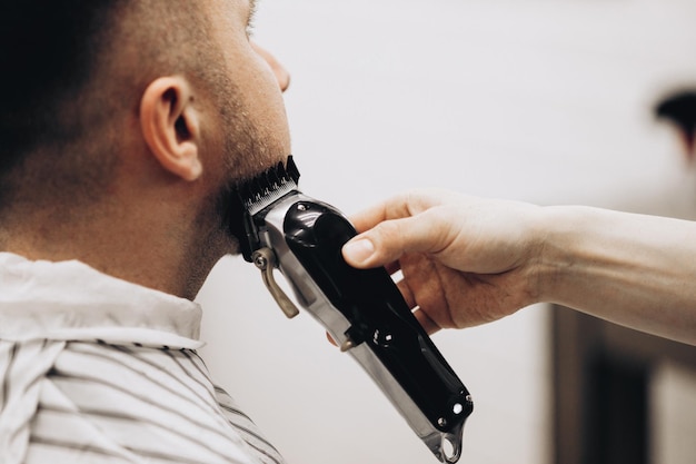 Barbeiro cortando barba para homem na barbearia emoldurando navalha elétrica vintage tingida de marrom