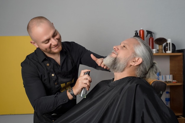 Barbeiro cortando e modelando a barba de um homem de cabelos grisalhos Barbearia para homens