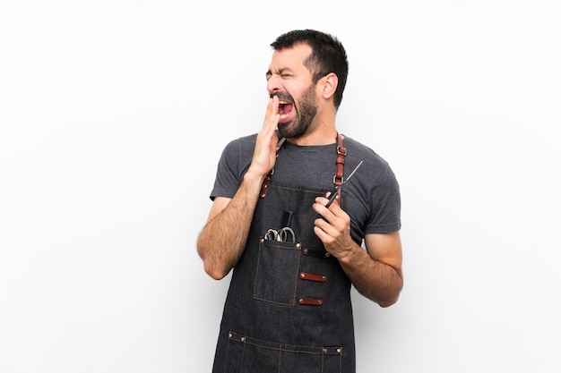 Foto barbeiro de avental bocejando e cobrindo a boca aberta com a mão