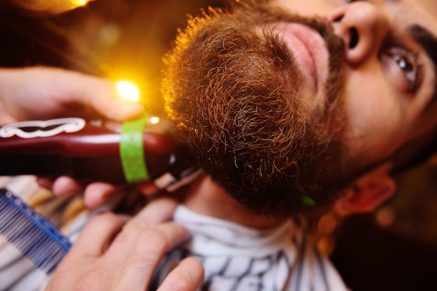 Barbeiro está moldando sua barba para o cliente na barbearia