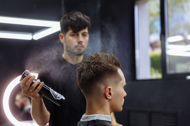 Barbeiro faz penteado com spray de cabelo após o corte de cabelo na barbearia.