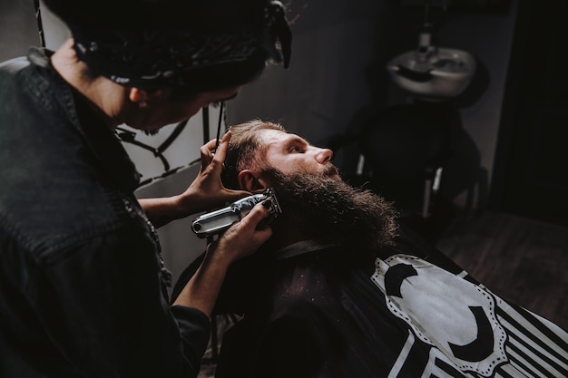 Barbeiro jovem fazendo corte de cabelo de homem barbudo na barbearia autocuidado beleza masculina cuidados com o cabelo s