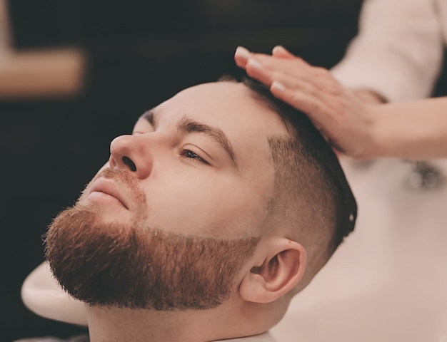 Barbeiro lavando o cabelo de um cliente barbudo em uma barbearia