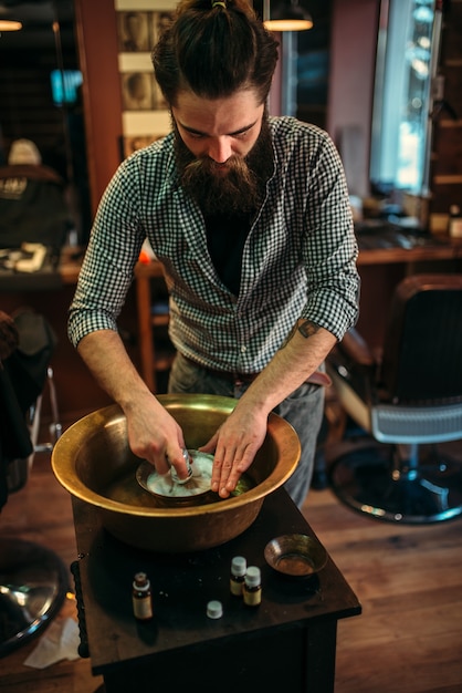 Barbeiro preparando espuma de barbear em uma tigela de cobre na barbearia.