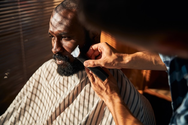 Barbeiro raspando a barba do cliente com o cortador elétrico em uma barbearia