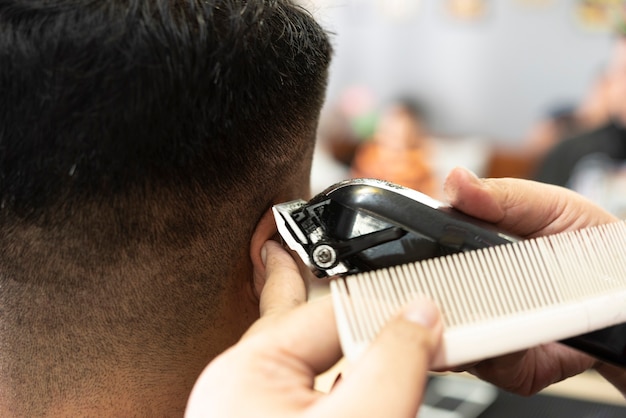 Barbeiro raspando cabelos com máquina de corte elétrica profissional em barbearia