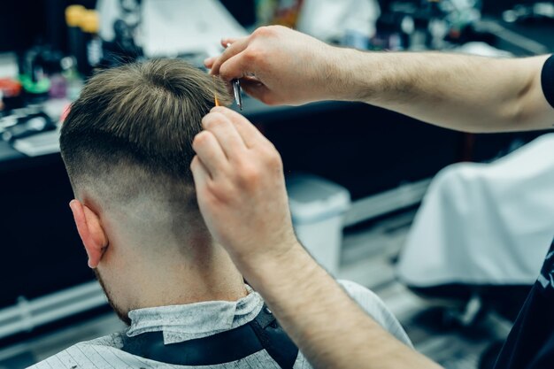 Foto barbeiro tatuado corta o cabelo do cliente com tesoura de perto homem atraente está recebendo um modo