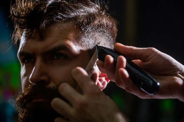 Barber arbeitet mit Haarschneidemaschine. Hipster-Kunde bekommt Haarschnitt. Hände des Friseurs mit Haarschneider. Haarschnitt-Konzept. Hipster-Kunde bekommt Haarschnitt. Mann, der Friseur im Friseursalon besucht.