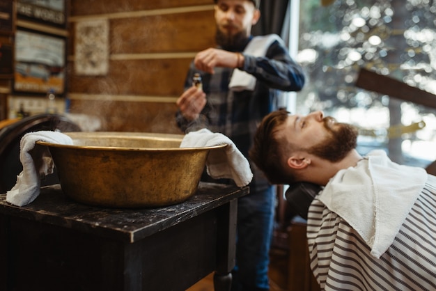 Barber encharca a toalha, cortando a barba. barbearia profissional é uma ocupação moderna