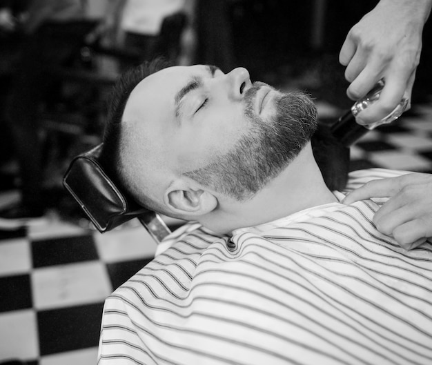 Barber limpia la barba de un hombre con un cepillo. concepto de peluquería