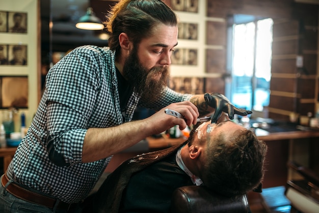 Barber raspa a barba do cliente raspando a lâmina na barbearia.