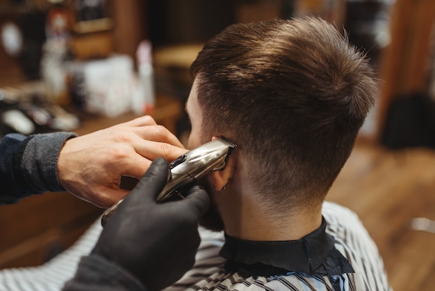 Barber segura o pente e corta o cabelo da cliente. A barbearia profissional é uma ocupação moderna. Cabeleireiro masculino e cliente em salão de estilo retro