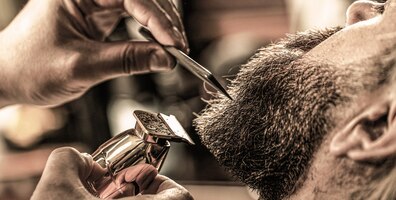 Barber trabalha com um cortador de barba. cliente hipster cortando cabelo. mãos de um cabeleireiro com um cortador de barba, closeup. homem barbudo na barbearia. homem visitando cabeleireiro na barbearia.