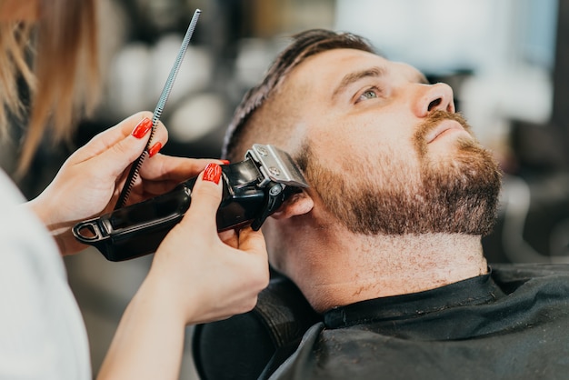 El barbero le corta la barba a un hombre brutal en el salón.