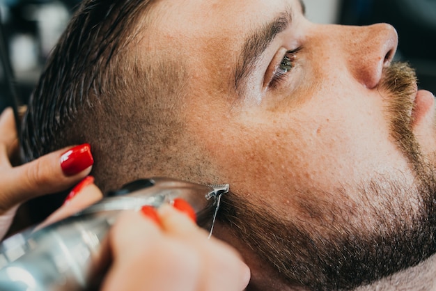 Foto el barbero le corta la barba a un hombre brutal en el salón.