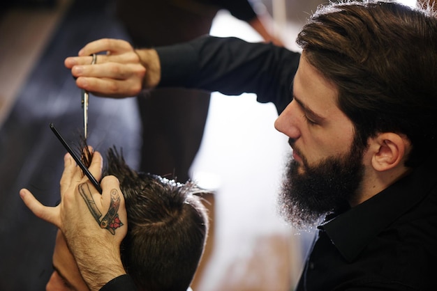 El Barbero un hombre con barba en proceso de cortarle al cliente unas tijeras en la Barbería