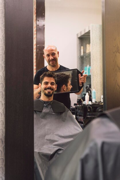 Foto barbero mostrando el espejo al cliente en el salón