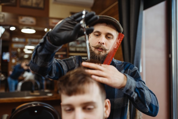 Barbero con peine y tijeras hace cortes de pelo con estilo a un cliente.