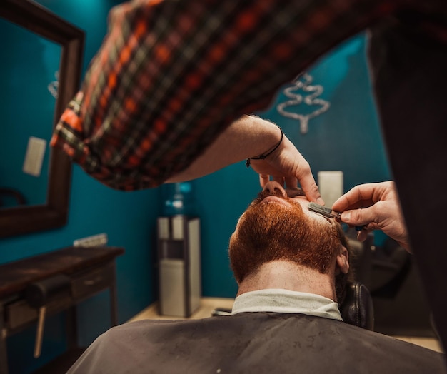 Un barbero profesional le corta la barba a un joven hipster