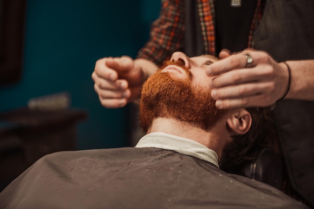 Un barbero profesional le corta la barba a un joven hipster