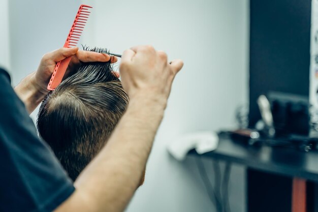 Foto el barbero tatuado corta el cabello del cliente con tijeras de cerca el hombre atractivo está teniendo un modo