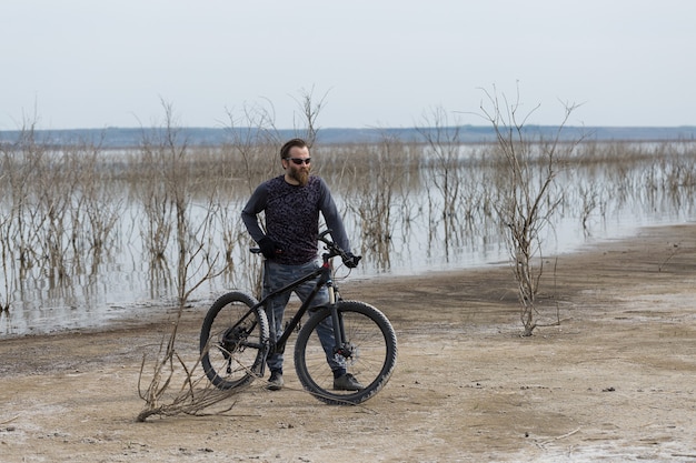 Barbudo brutal de esportes em uma bicicleta de montanha moderna. um ciclista em um lugar deserto de sal à beira do lago.