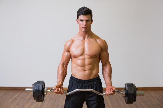 Barbudo de elevación del hombre muscular descamisado en gimnasio