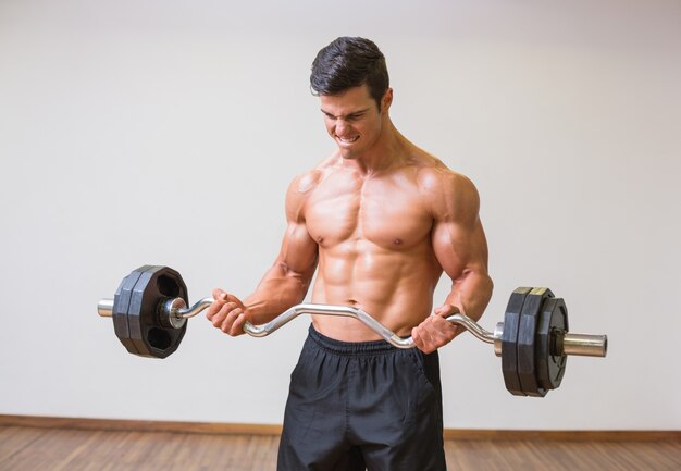 Barbudo de elevación del hombre muscular descamisado en gimnasio